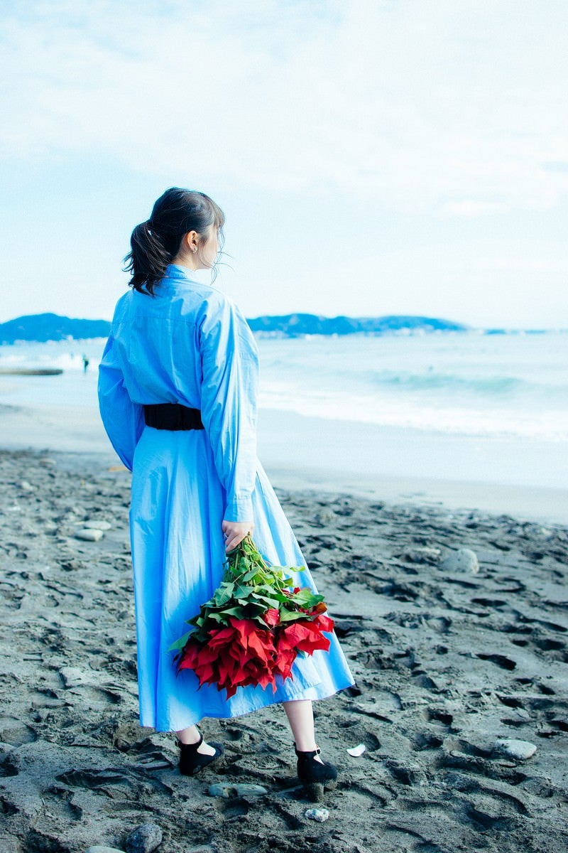 「波打ち際で赤い花束を手にする女性」の写真
