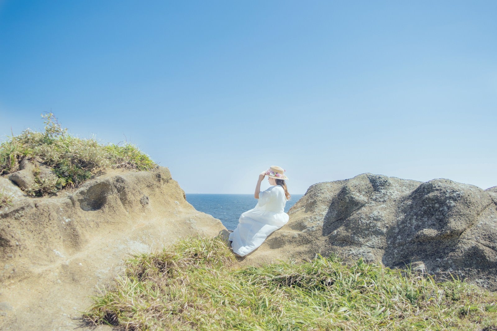 「海岸に腰を下ろし海を見つめる女性」の写真