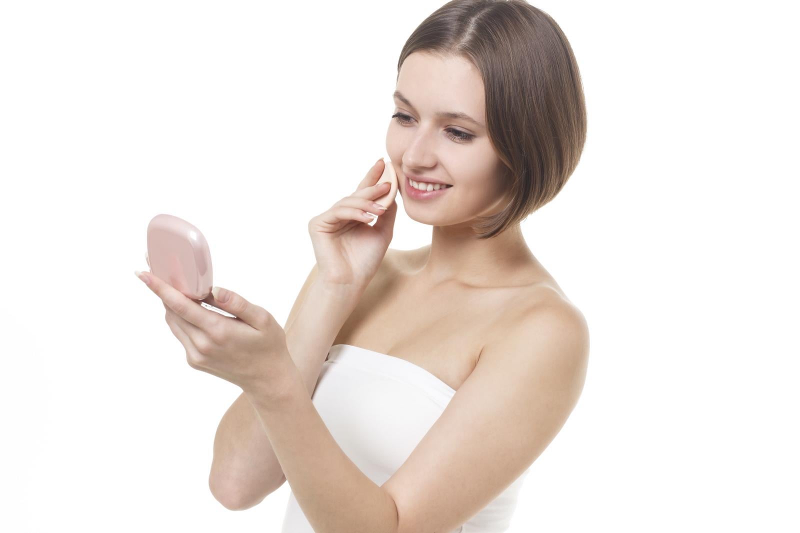 ピンク色のコンパクトミラーを見ながら化粧直しをするチューブトップ姿の女性［モデル：モデルファクトリー］