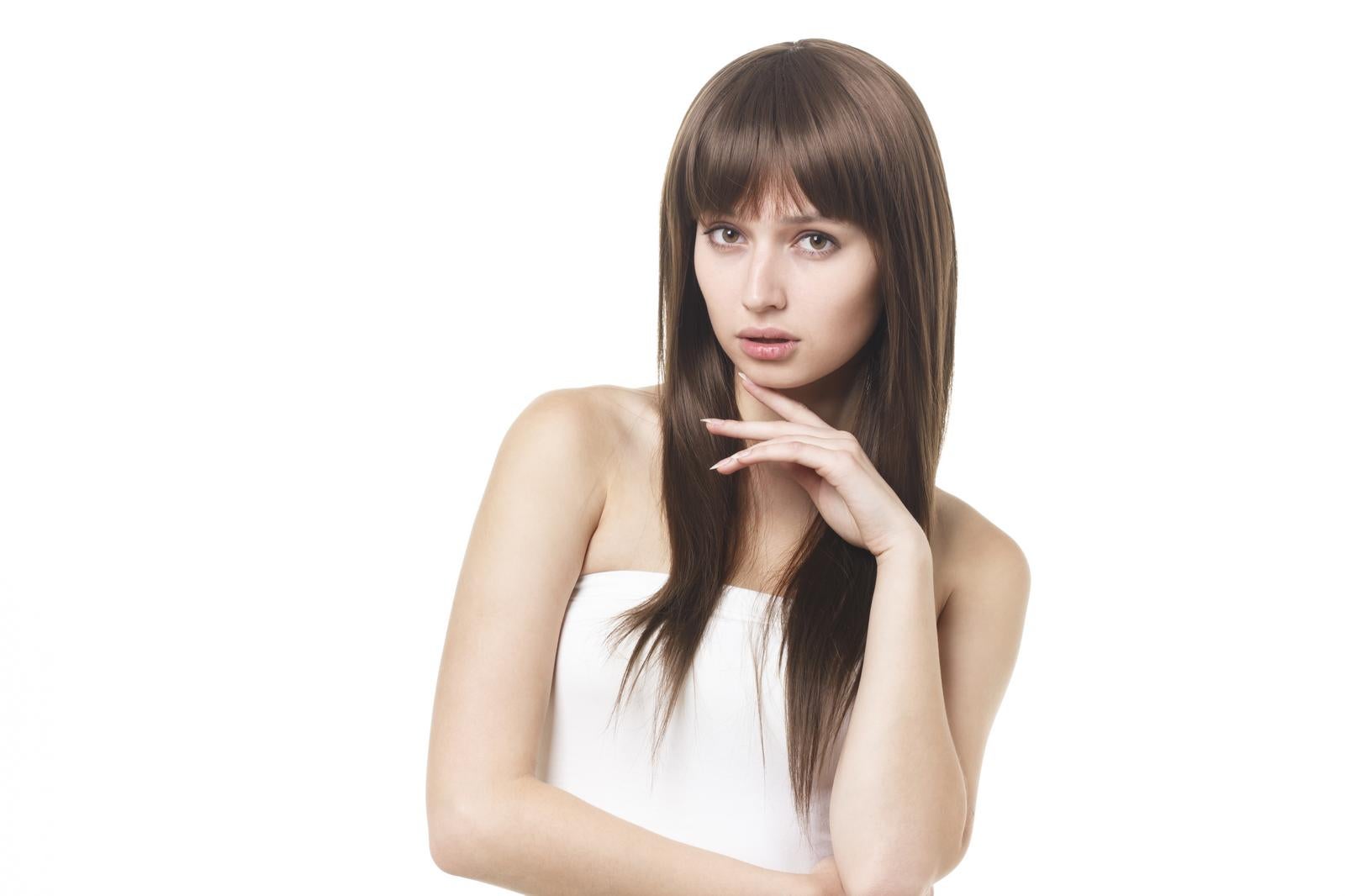 白背景でブラウンのストレートロングヘアの女性モデルがあごに手を添えてポーズをとっている［モデル：モデルファクトリー］