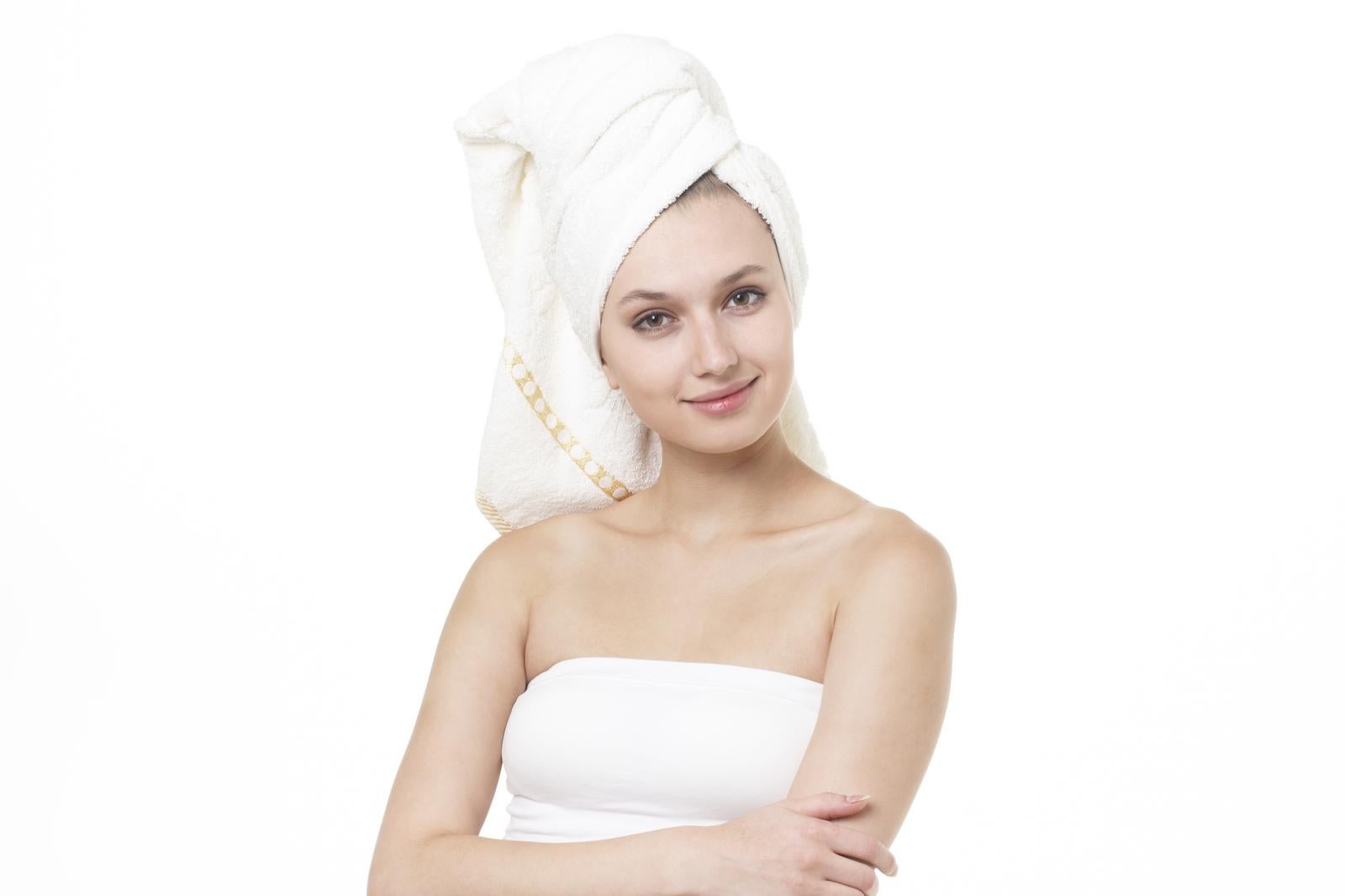 Woman after bath smiling, wearing white bath towel wrapped around head and white tube top