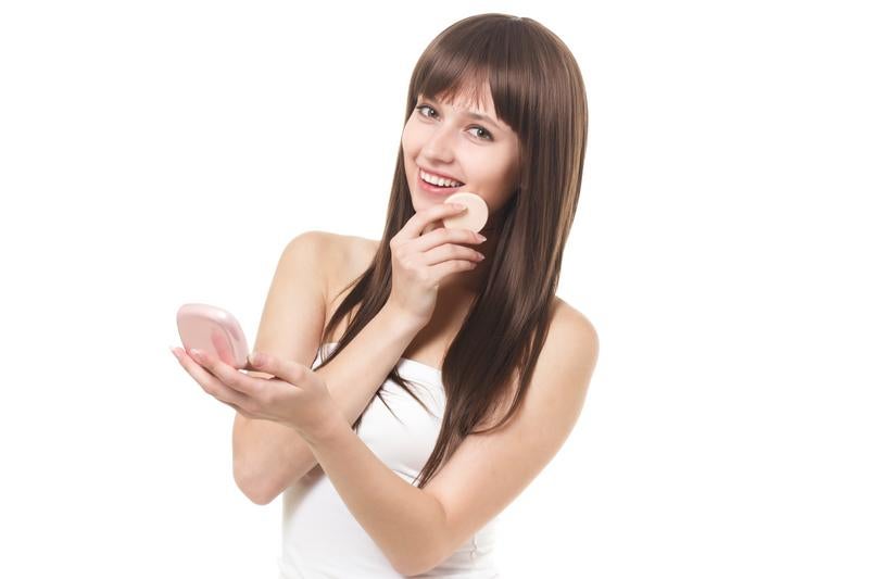 白いキャミソールを着て手鏡を見ながら微笑む女性の写真