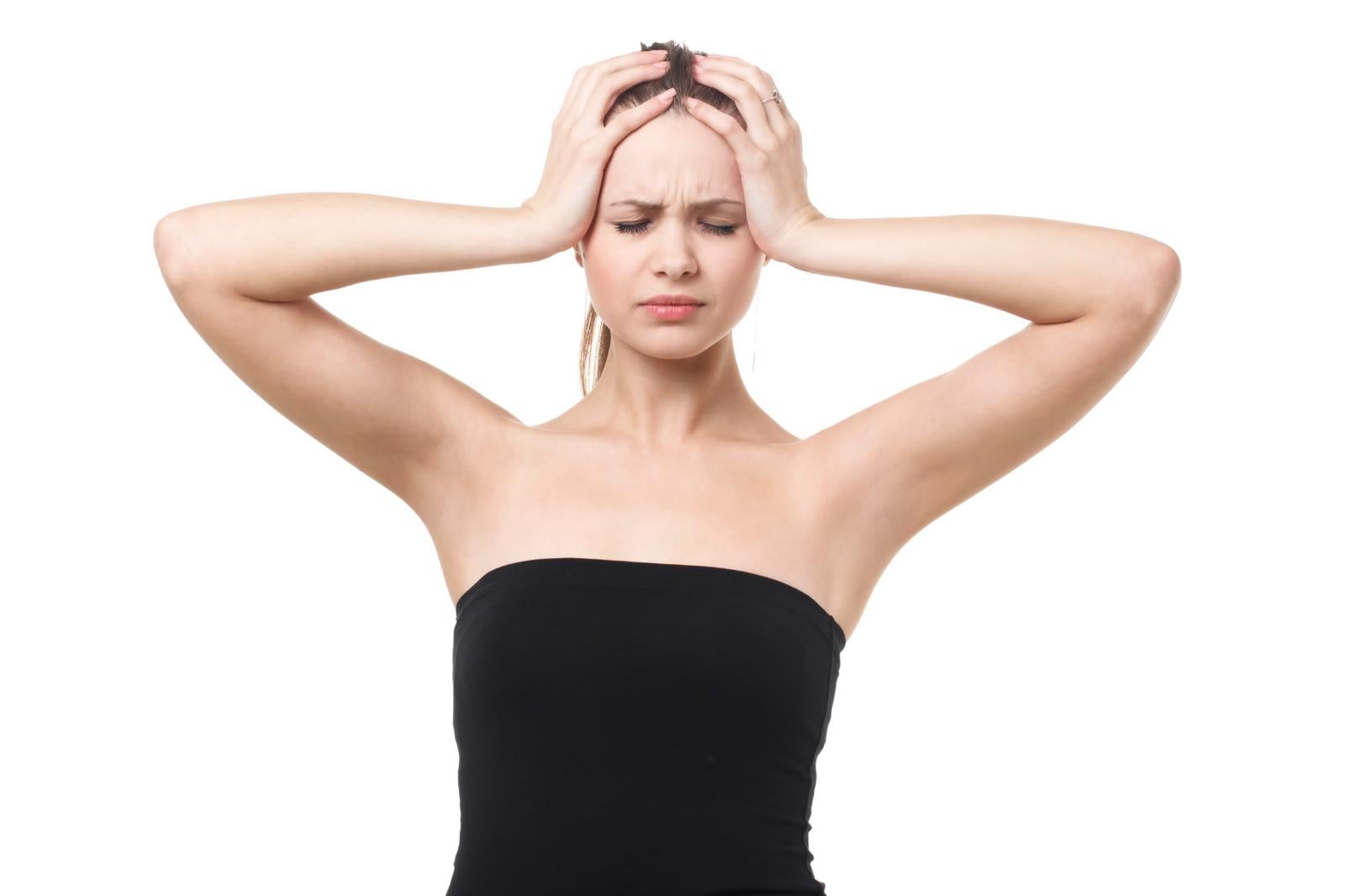Woman in black bare top holding her head with both hands against white background with eyes closed and a distressed expression