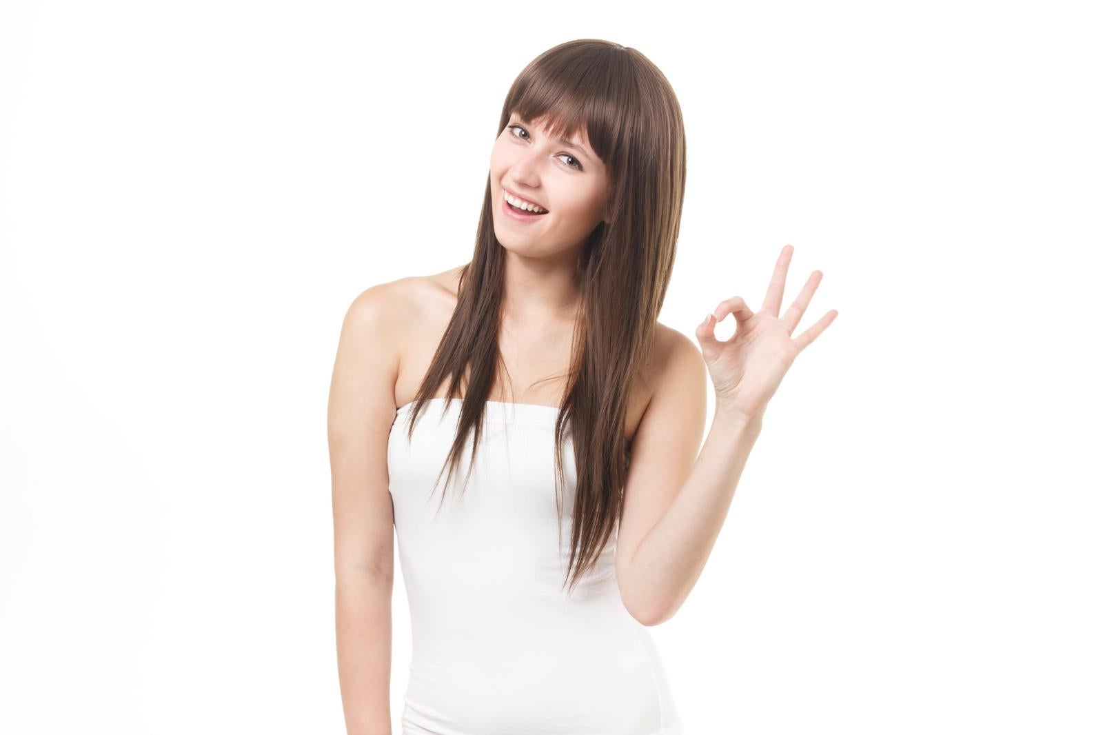 白いベアトップを着た長髪の女性が笑顔でOKサインをするポーズ［モデル：モデルファクトリー］