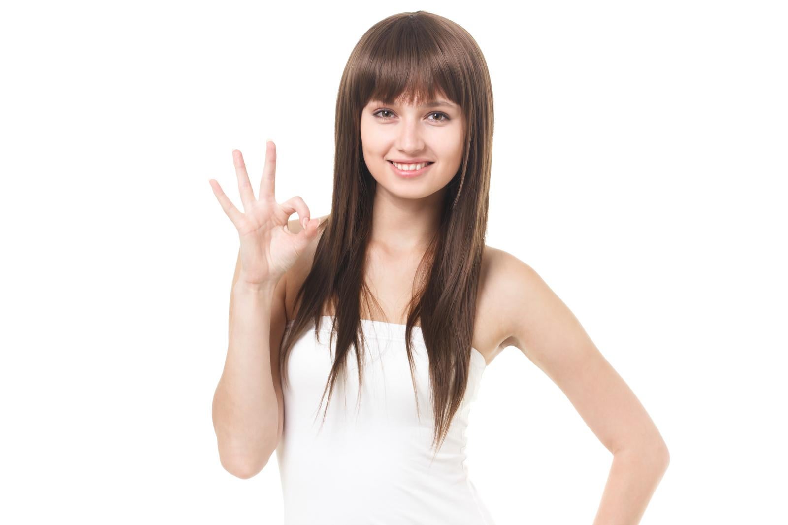 白背景の前でOKサインを出しながら笑顔でポーズをとるロングヘアの女性［モデル：モデルファクトリー］