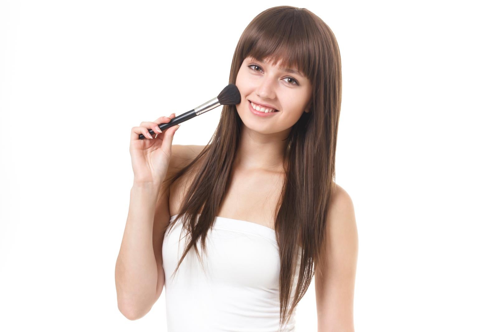 黒いハンドルのメイクブラシを肩に担ぐ、白いトップスを着た笑顔の女性のポートレート［モデル：モデルファクトリー］