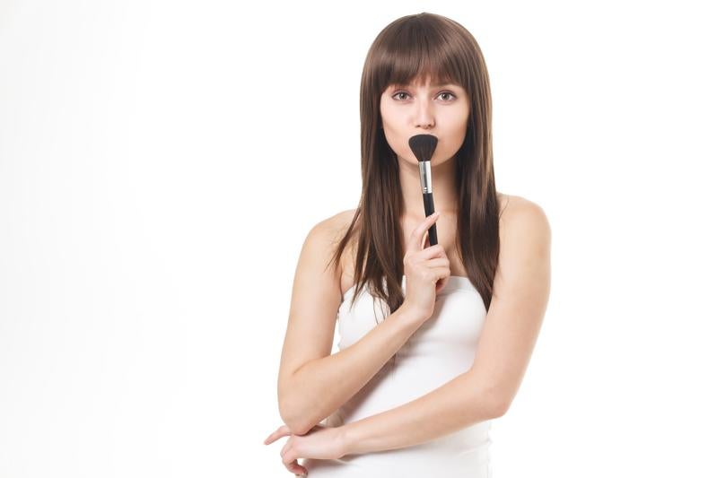 メイクブラシを口元に当てて上を見つめる女性の写真