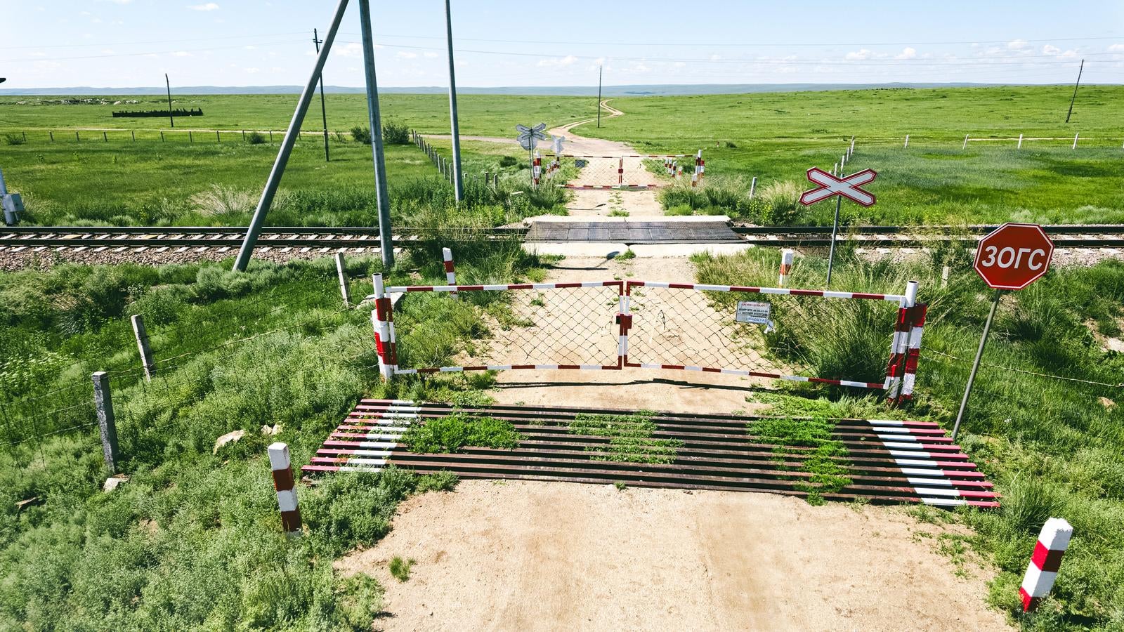 モンゴルの大草原を横切る線路の踏切と地平線まで続く未舗装の一本道