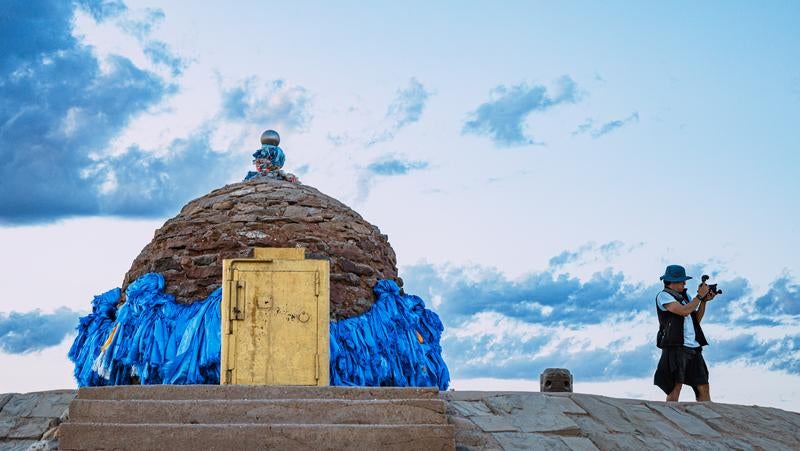 ▲石造りの塔を背にカメラを構える旅人の写真