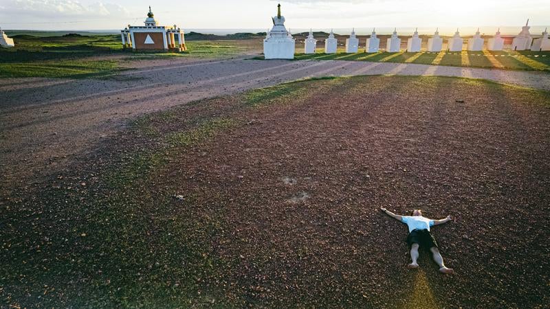 赤い土に寝そべって大地のエネルギーを吸収する旅行系YouTuberの写真