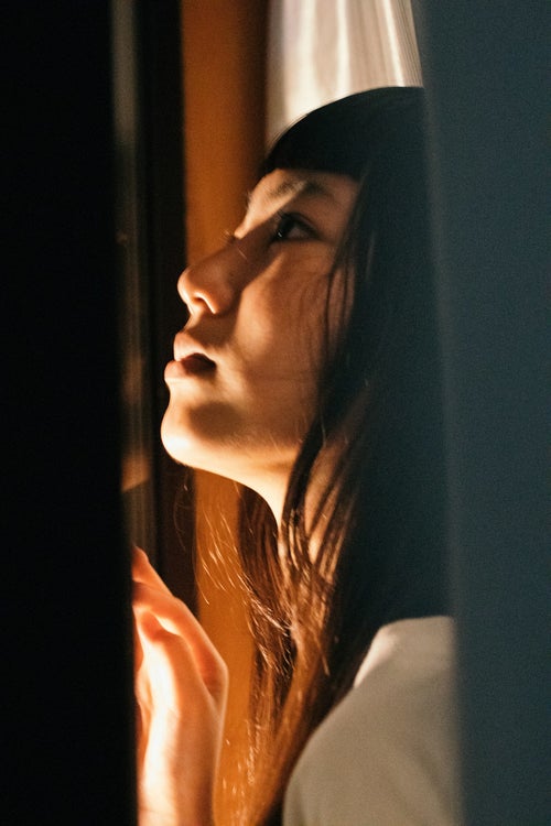夜に窓の外を見上げる女性の写真