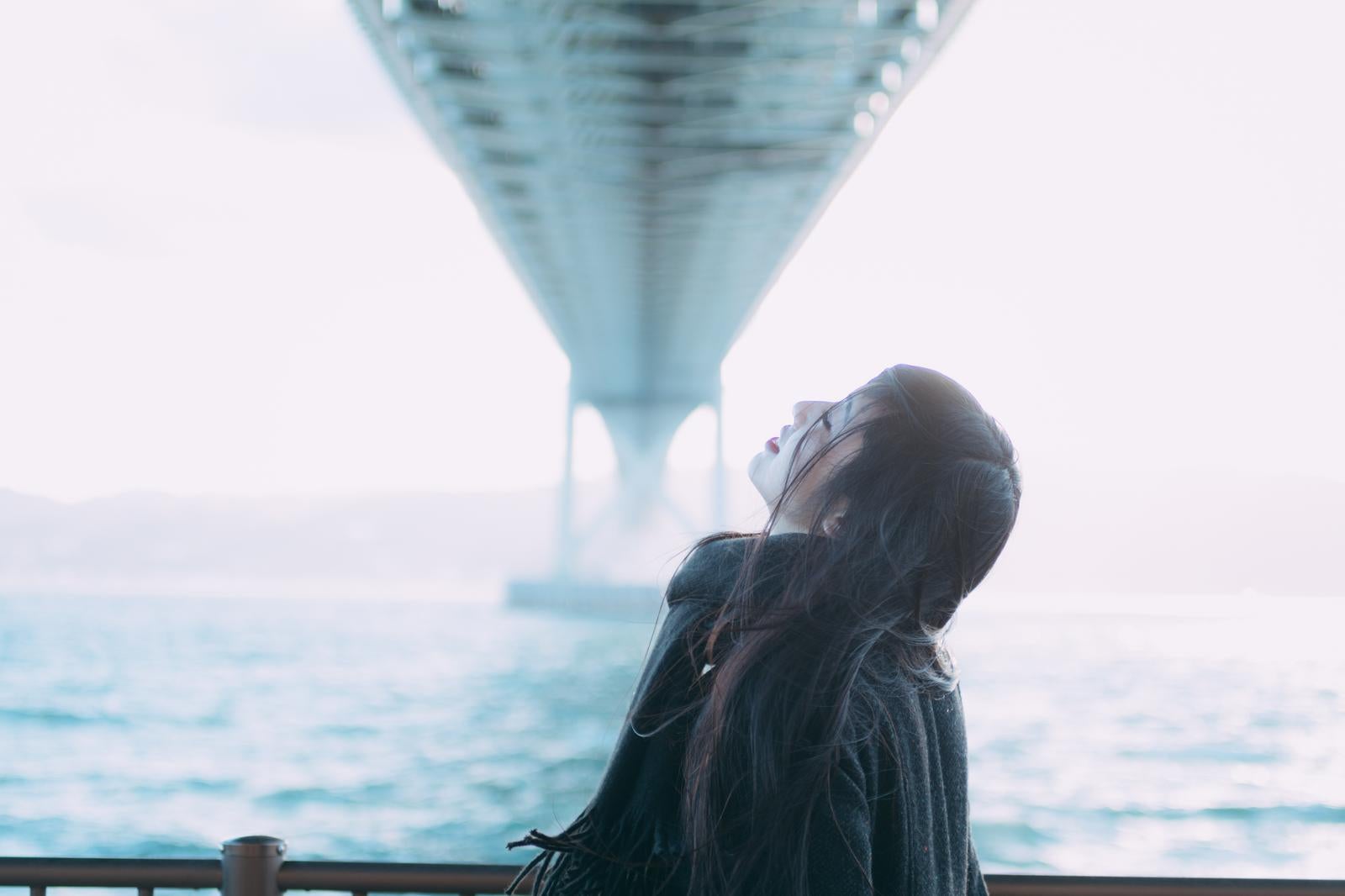 「海と橋を背景に空を見上げる女性の美しいポートレート」の写真［モデル：なんこ］