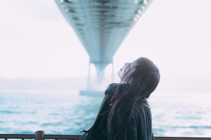 海と橋を背景に空を見上げる女性の美しいポートレートの写真