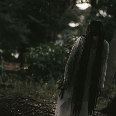 薄明るい森の中を徘徊する女性の写真