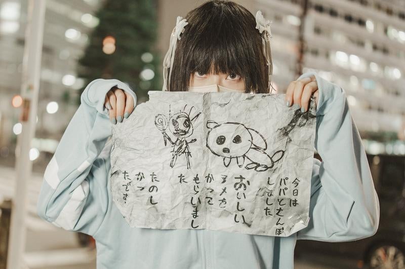 黒髪の子どもが手描きの怪文書イラストを両手で掲げているの写真