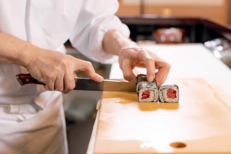 寿司職人がまな板の上で鉄火巻を切り分ける様子の写真