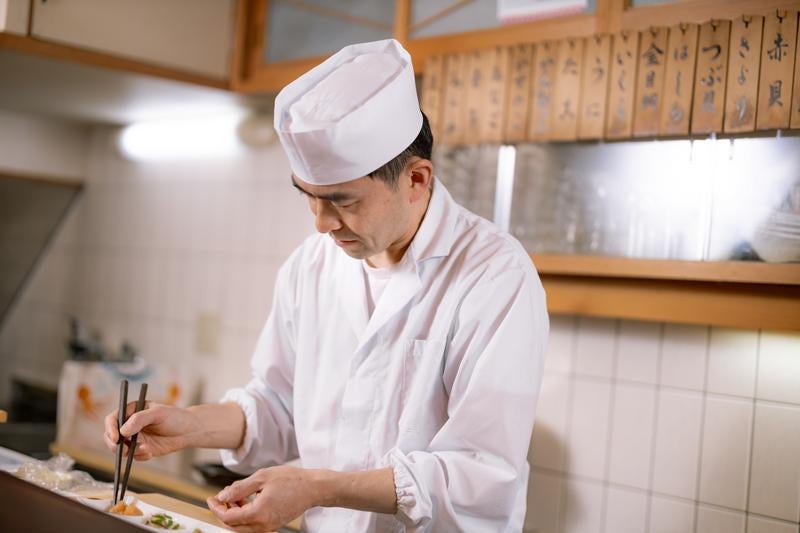 寿司職人がカウンター越しに箸を使って盛り付けする様子の写真
