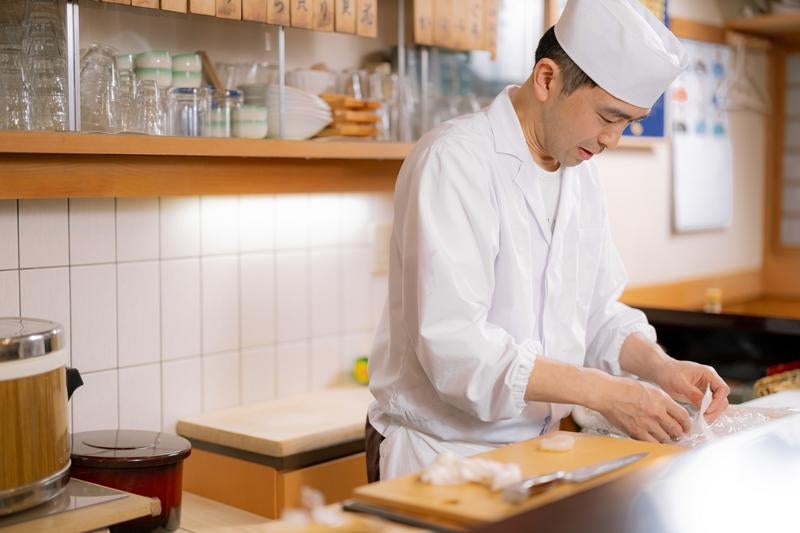 寿司職人が白い調理服と帽子を着て調理する様子の写真