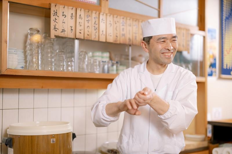 にこやかな笑顔で寿司を握る店主の写真