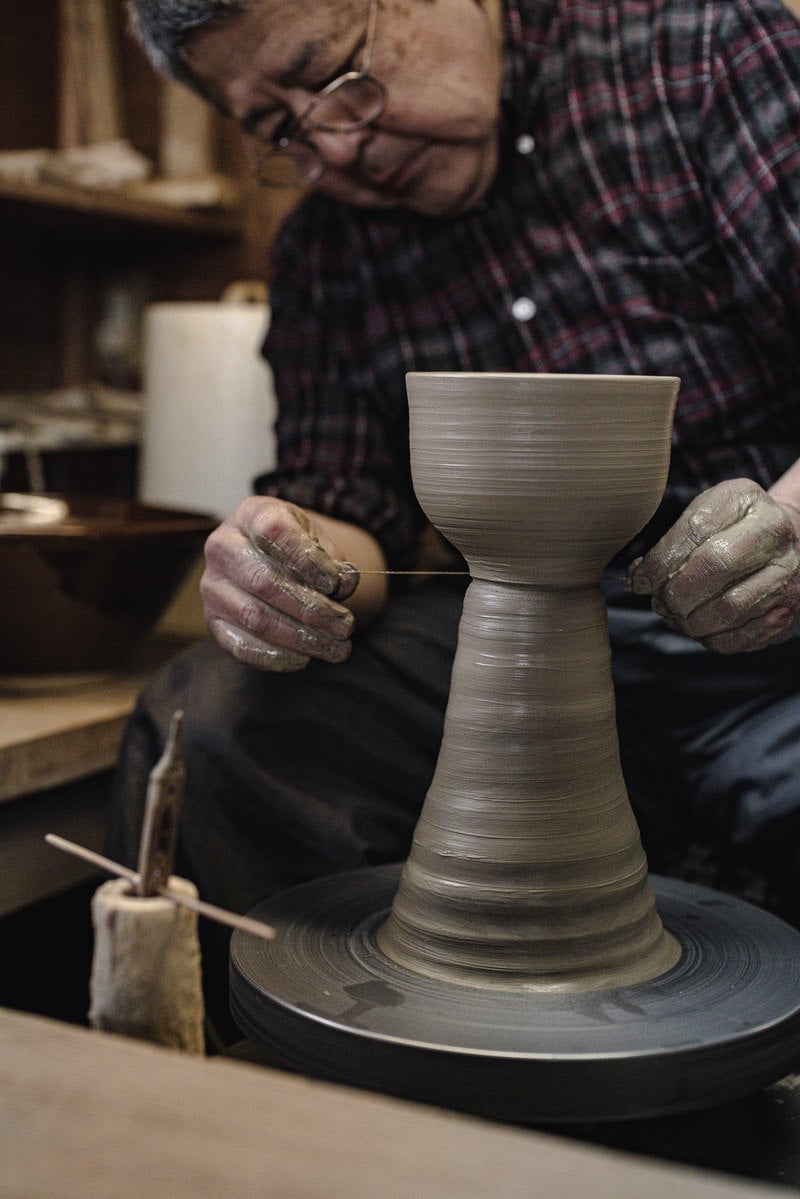 「整形した陶器をろくろ台から糸切りする職人の様子」の写真［モデル：モデルリリース］