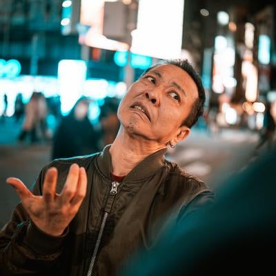 ネオン看板が光る繁華街で感情的に怒りをあらわにする男性の写真