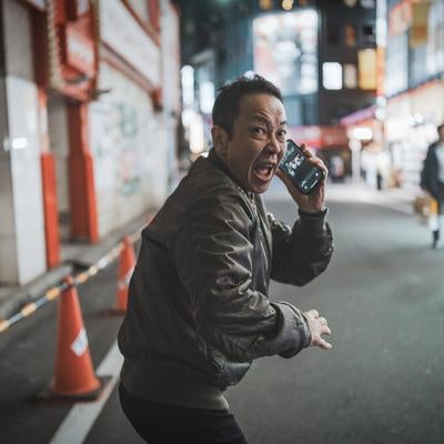 夜の繁華街で電話を握りながら振り返る男性の逃走シーンの写真