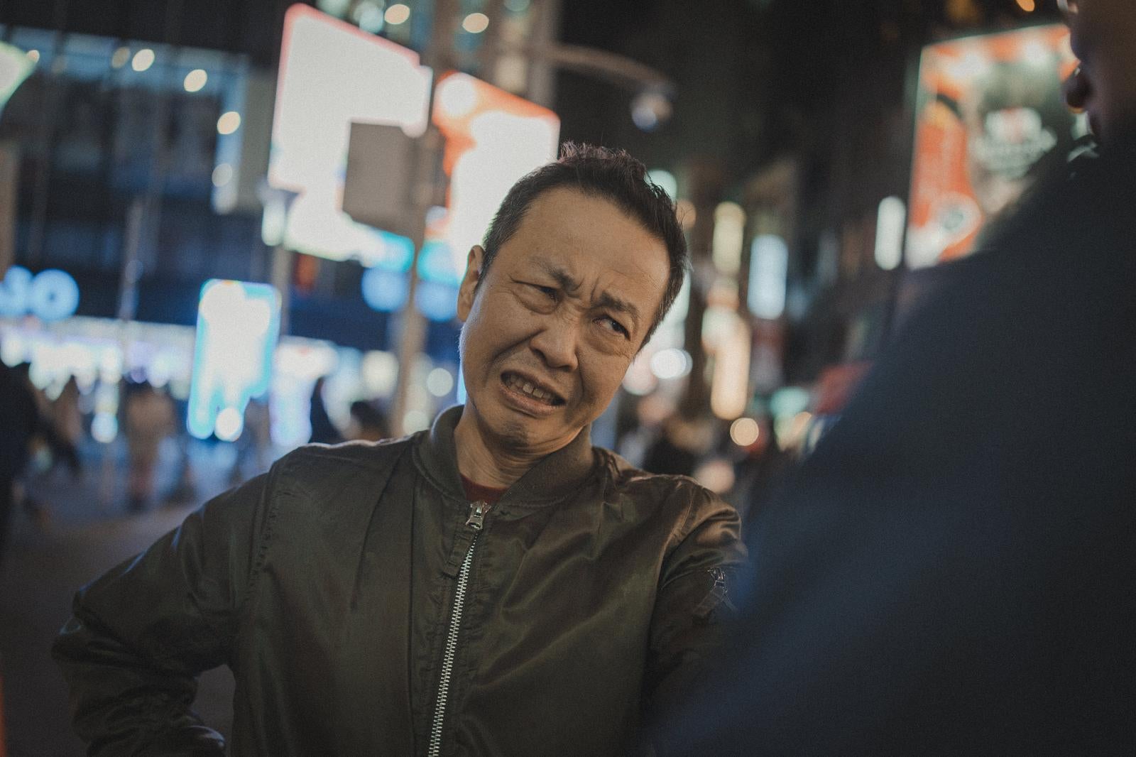 夜間の街中で眉をひそめ歯を食いしばって怒る男性［モデル：のせさん］