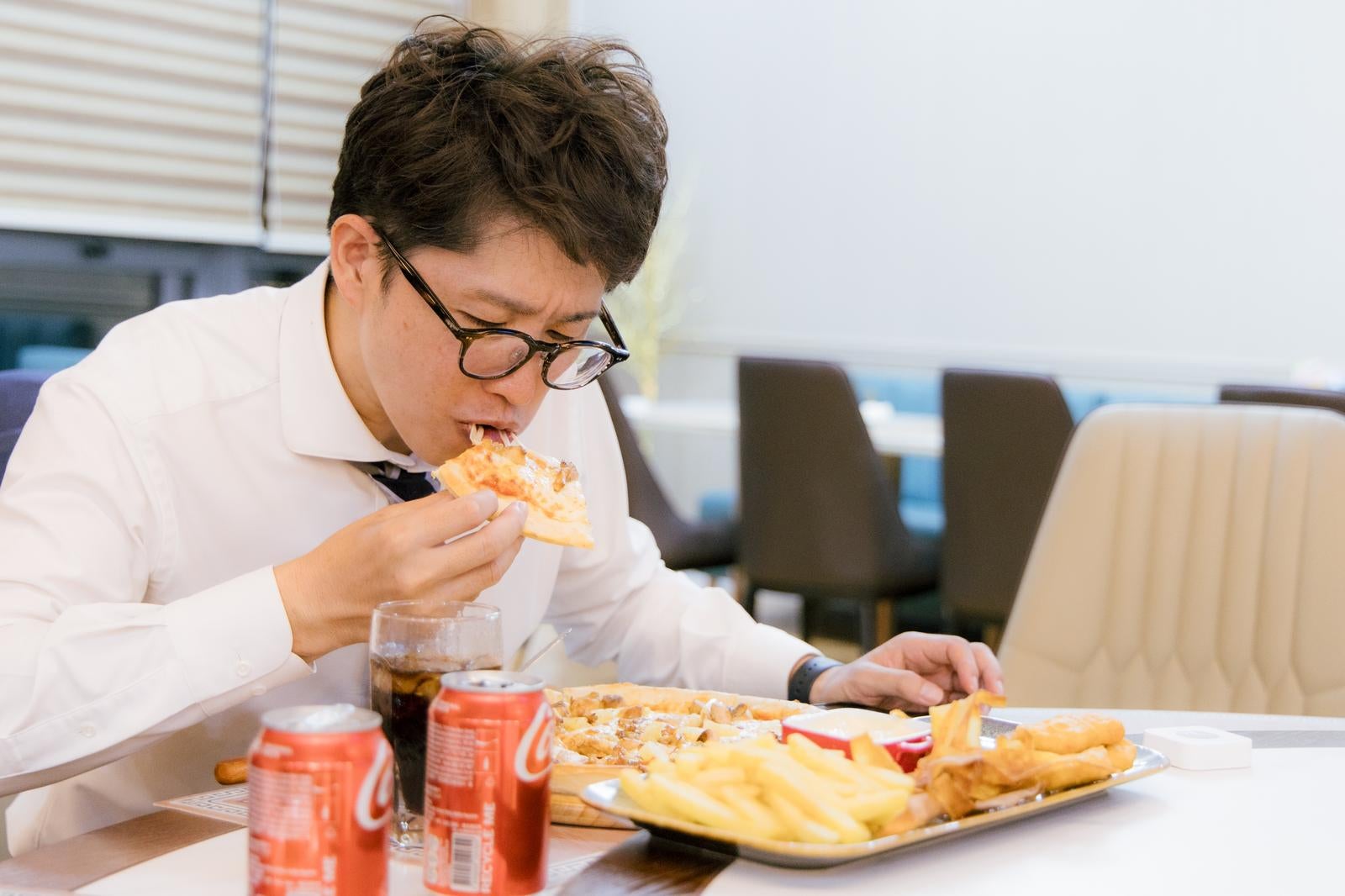 「残業後にピザとコーラを縛食いする会社員」の写真［モデル：野崎繁裕］