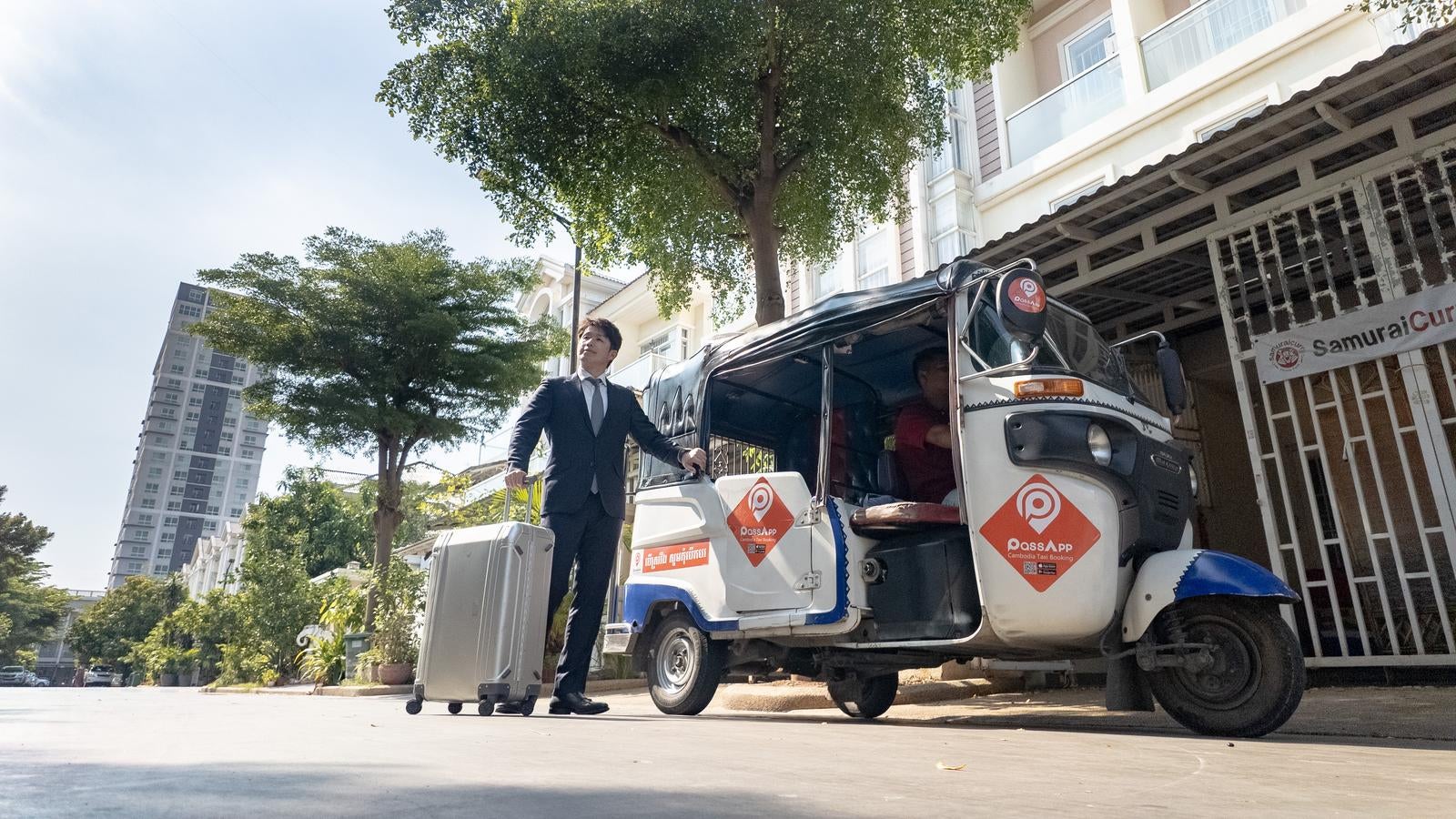 「カンボジアのトゥクトゥクに乗って出発するビジネスマン」の写真［モデル：野崎繁裕］