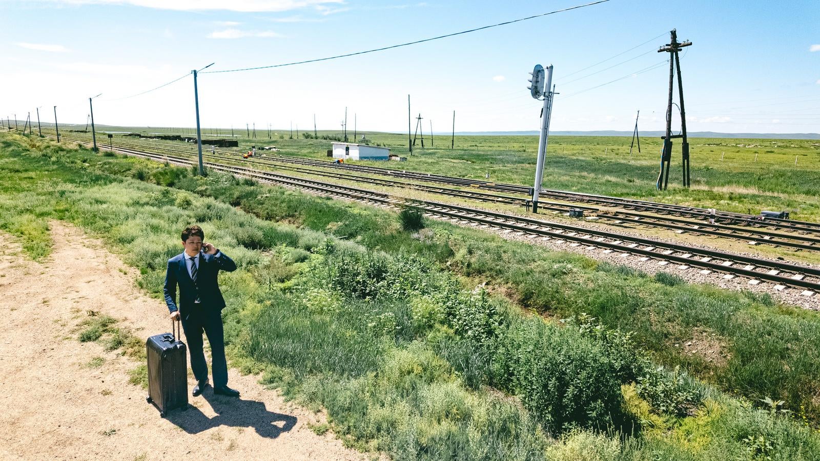 「広がる草原と線路を前に商談するビジネスマン」の写真［モデル：野崎繁裕］