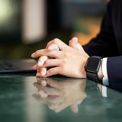 スマートウォッチを着けて手を組むビジネスマンの写真