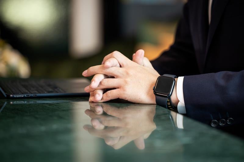 スマートウォッチを着けて手を組むビジネスマンの写真