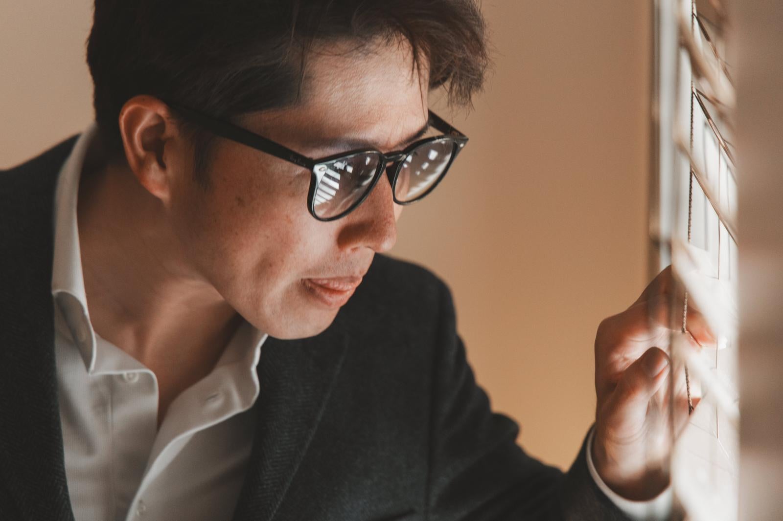 「ブラインドの隙間から覗き込む捜査官風の様子の男性の撮影」の写真［モデル：野崎繁裕］