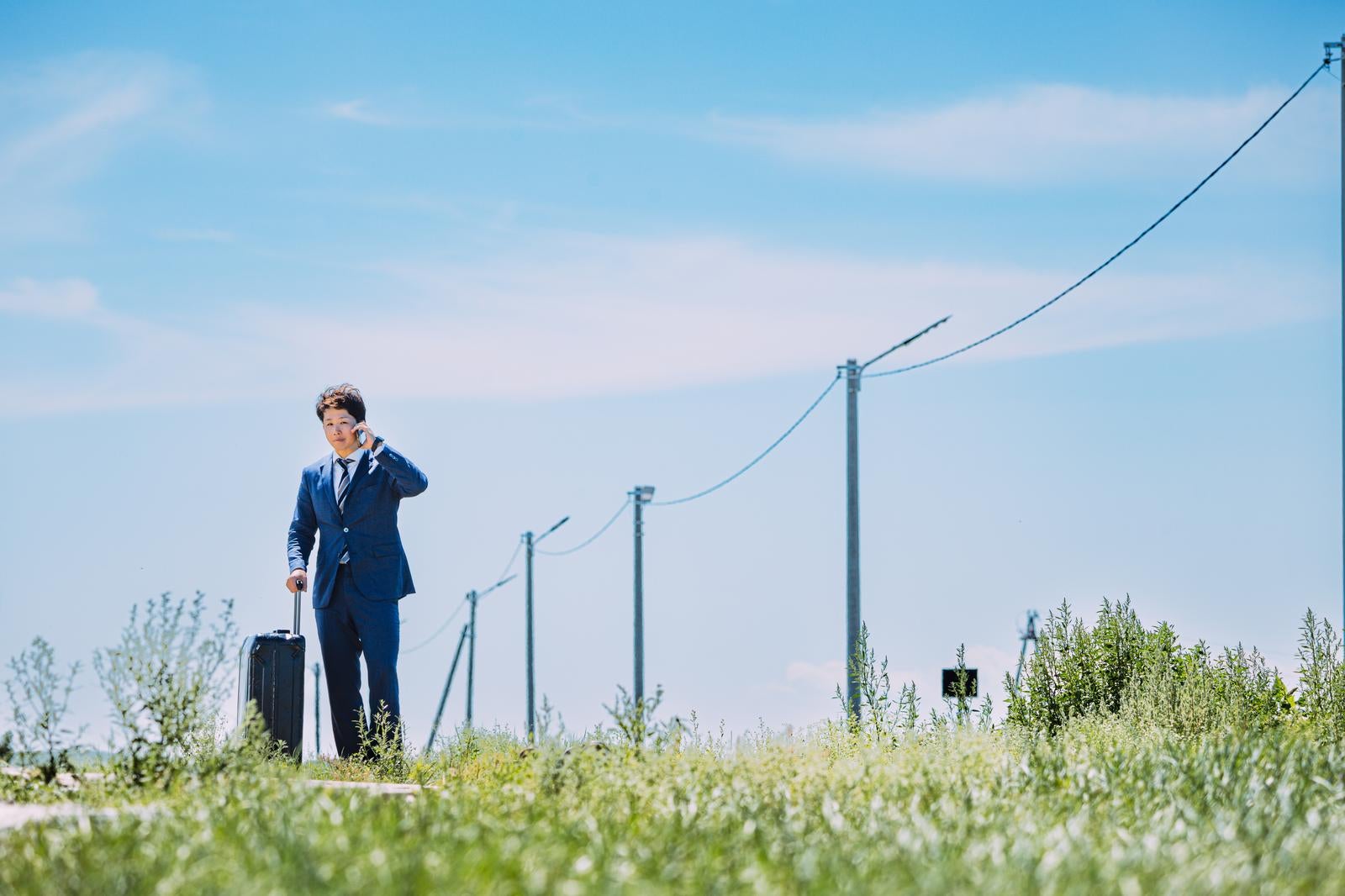 「広大な自然の中で電話するビジネスマン」の写真［モデル：野崎繁裕］