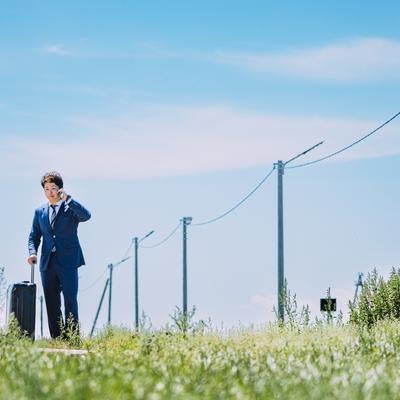 広大な自然の中で電話するビジネスマンの写真