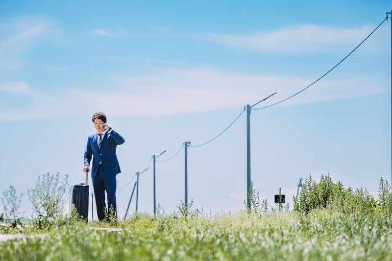 広大な自然の中で電話するビジネスマンの写真