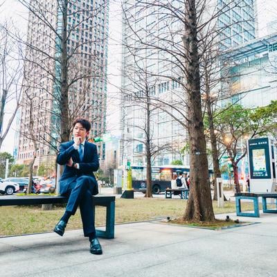 高層ビルに囲まれたベンチで一息つくビジネスマンの素材
