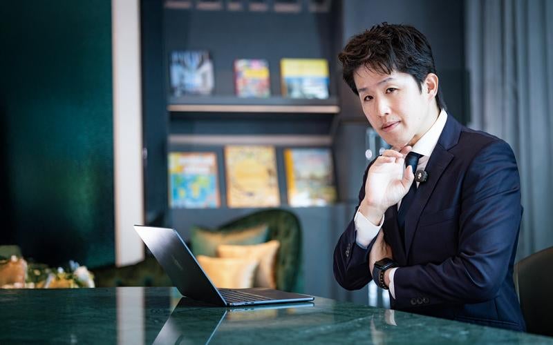 書棚のある落ち着いたワークスペースで頬杖をつきながら思考するビジネスパーソンの写真