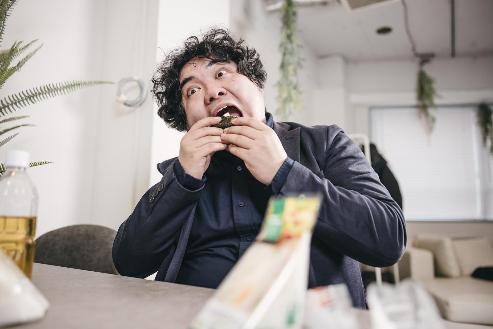 「大口を開けておにぎりを食べる男性」の写真［モデル：段田隼人］