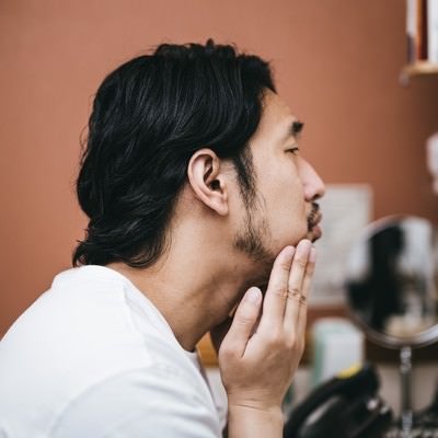 髭面の男性が洗面所で行う今日はお肌の調子がイマイチな朝のスキンケアの写真