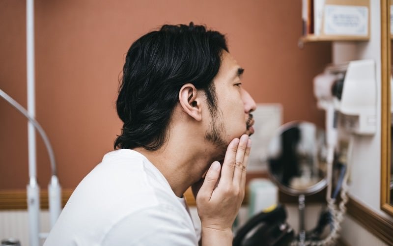 髭面の男性が洗面所で行う今日はお肌の調子がイマイチな朝のスキンケアの写真