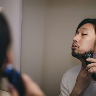 鏡を見ながらシェーバーで髭剃り中の写真
