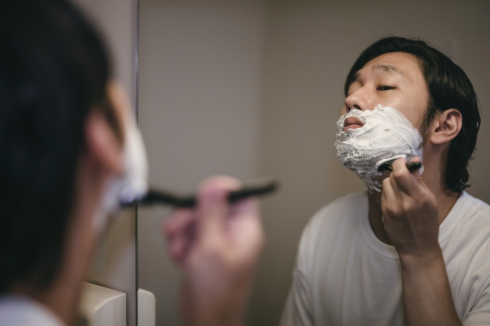 「シェービングクリームを塗って顎から髭を剃る男性」の写真［モデル：大川竜弥］