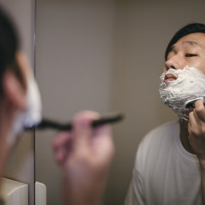シェービングクリームを塗って顎から髭を剃る男性の写真