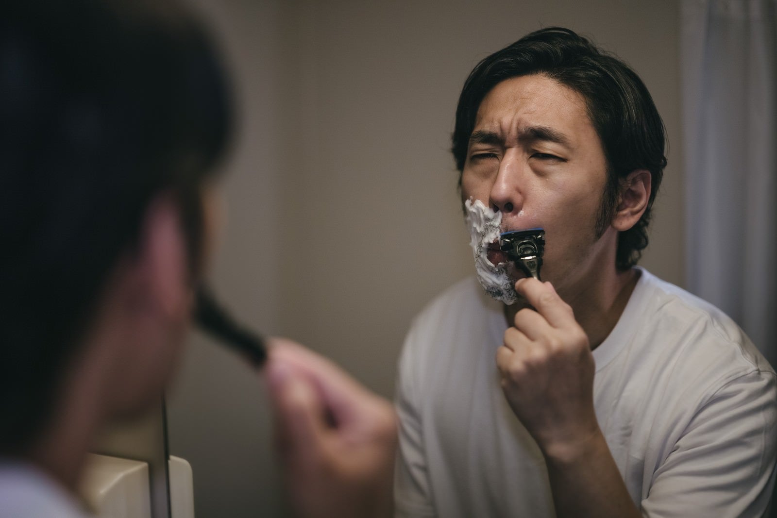 「しかめっ面して鼻下を剃る男性」の写真［モデル：大川竜弥］