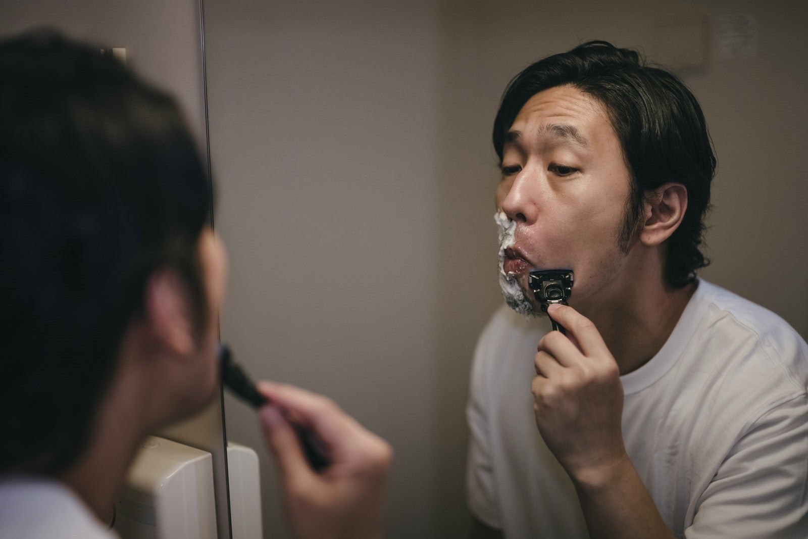 「鏡を見ながら髭を剃る男性」の写真［モデル：大川竜弥］