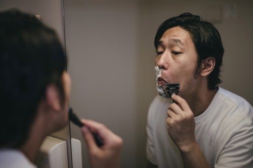 鏡を見ながら髭を剃る男性の写真
