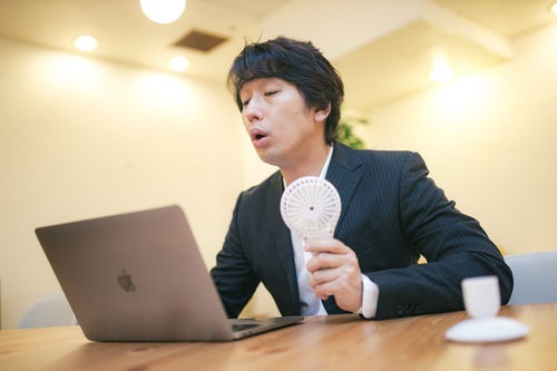 オンライン会議中にハンディ扇風機を使用する男性の写真