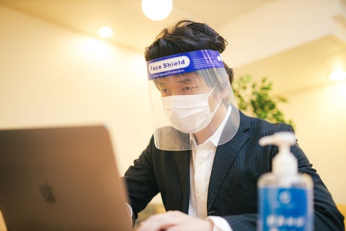 オンライン会議中もフェイスシールドとマスクを装着する男性の写真