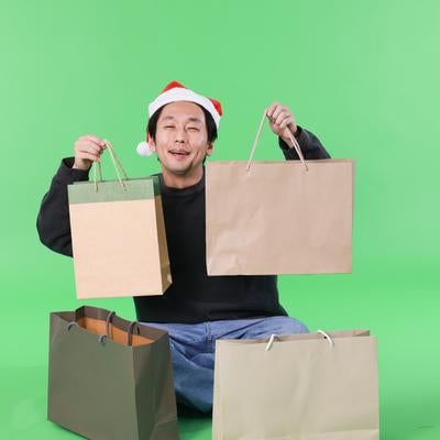 クリスマスセールで買い物しまくる男性（グリーン背景）の写真